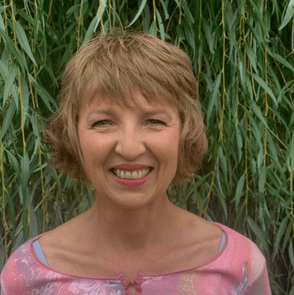 Woman with short hair smiling in front of green foliage.