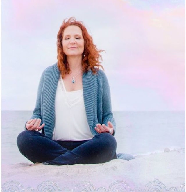 Woman meditating peacefully on the beach with eyes closed.